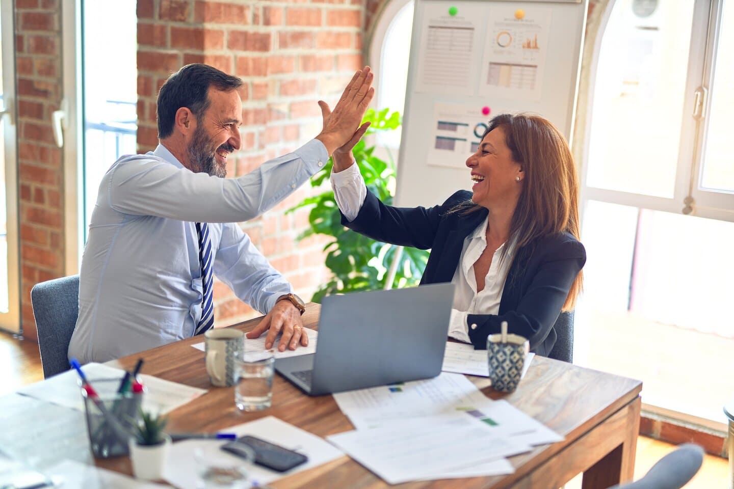 Two business owners giving high five at the office, smiling happy and confident